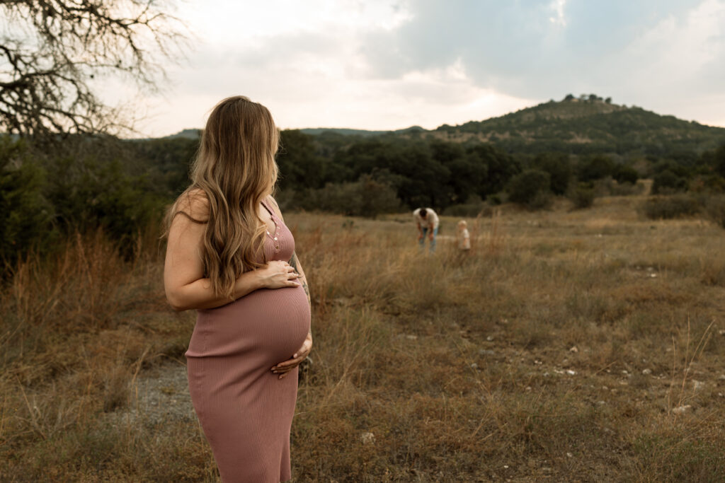 pregnant woman holding belly while looking at father and son in the distance