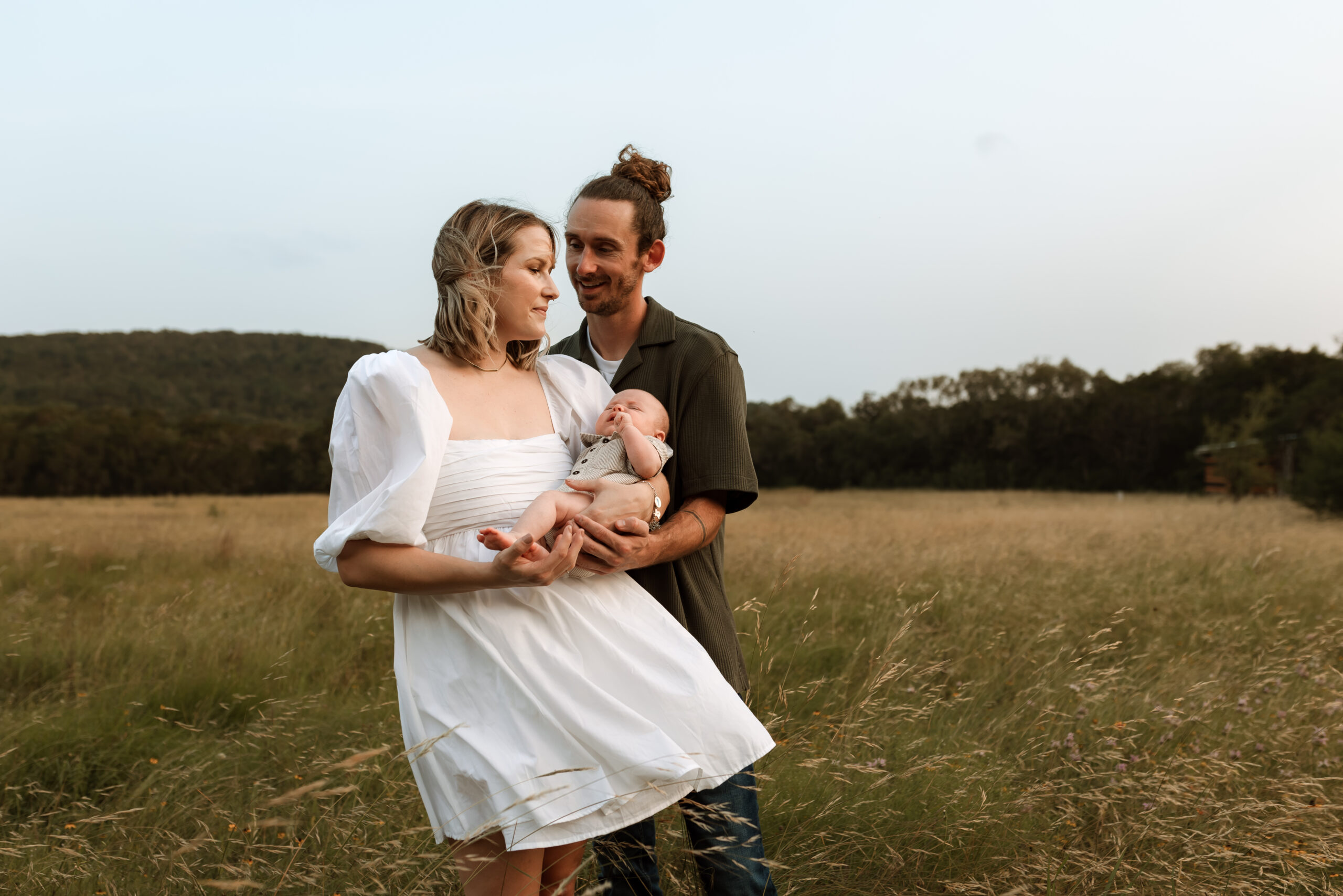 mom and dad holding baby in a field