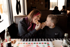 mom and son eating a slice of pizza during a family photo session at a local pizzeria