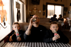 dad and sons drinking soda from glass coca cola bottles during family photo session at a local pizzeria