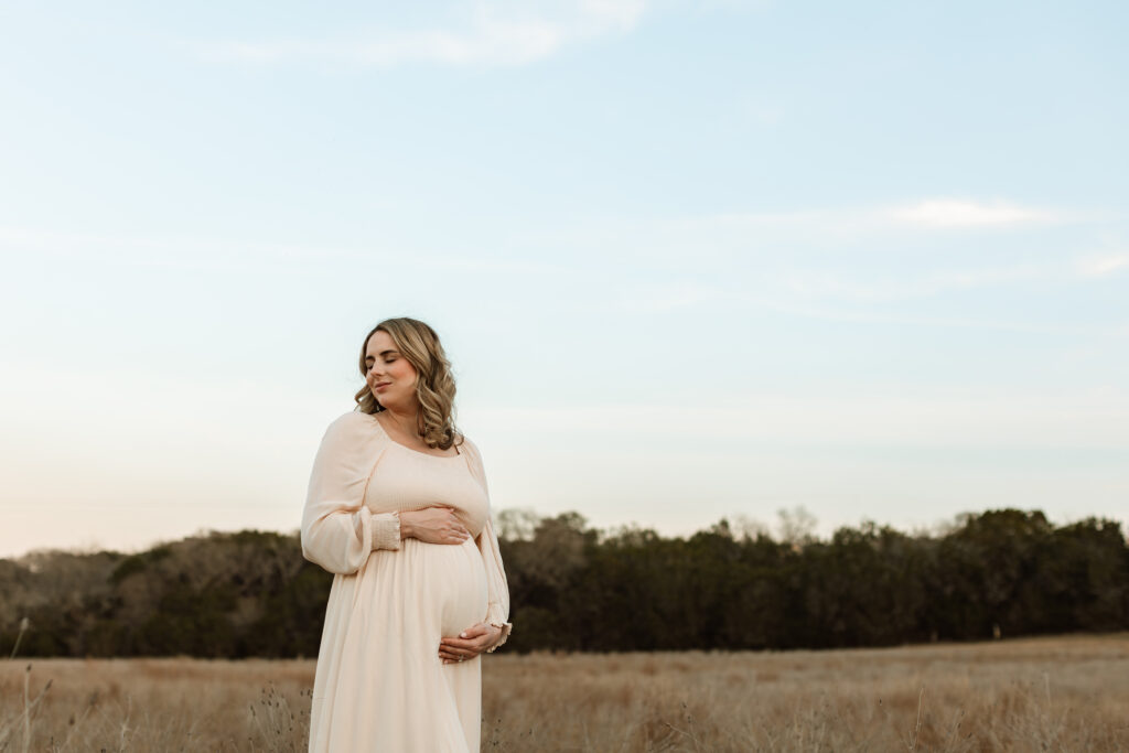 Pregnant woman holding her belly while standing in a field