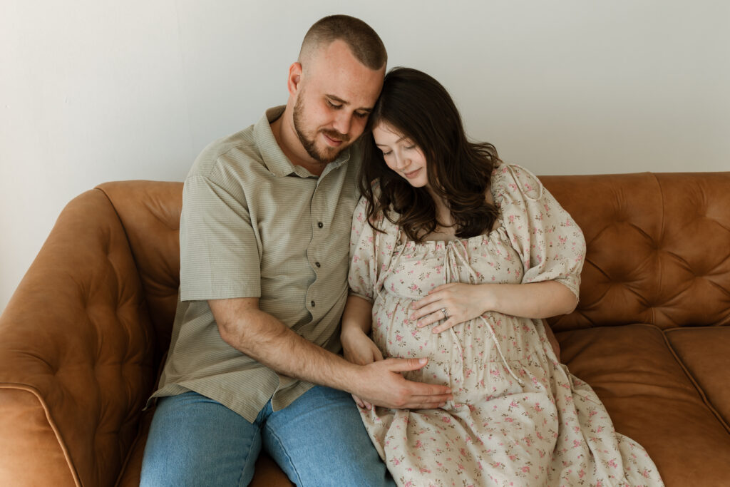 man and pregnant woman sitting on a couch in a studio for maternity photos