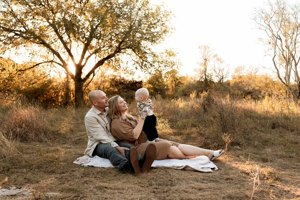 mom and dad sitting with 6 month old baby boy in a park